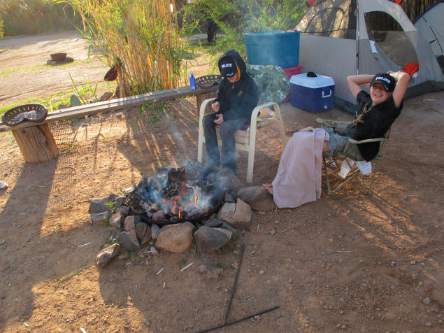 The boys warm themselves in front of the fire.